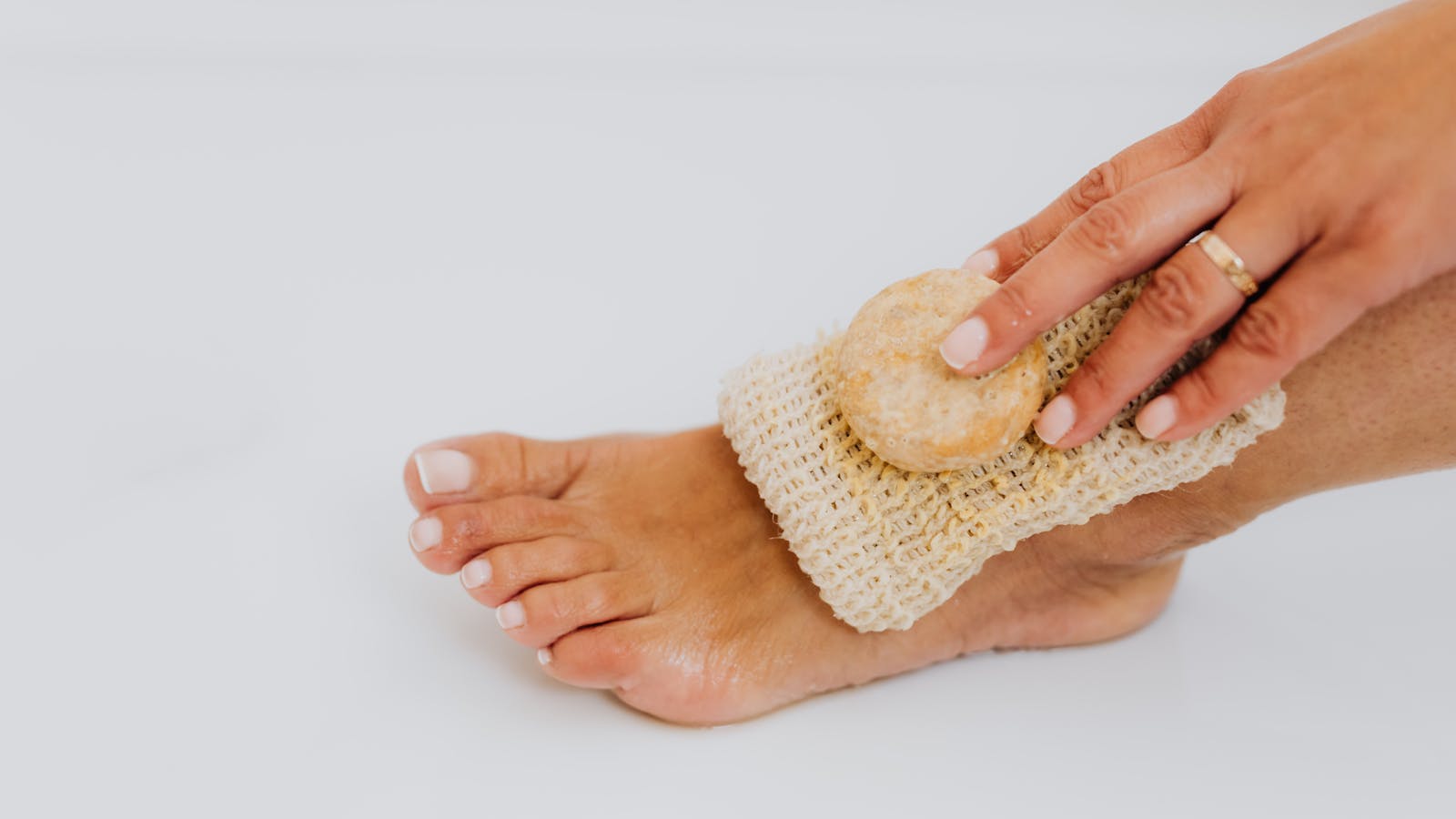 A hand using a textured scrub on the top of a bare foot during a home foot care routine.