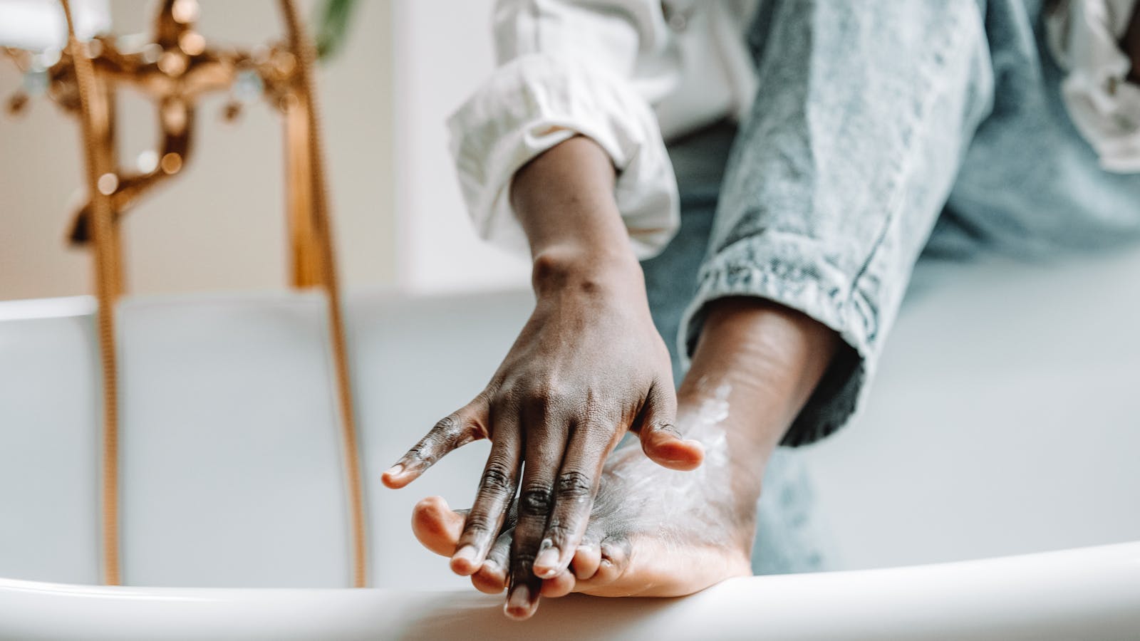 A person applying moisturizer to the top of a bare foot at home.