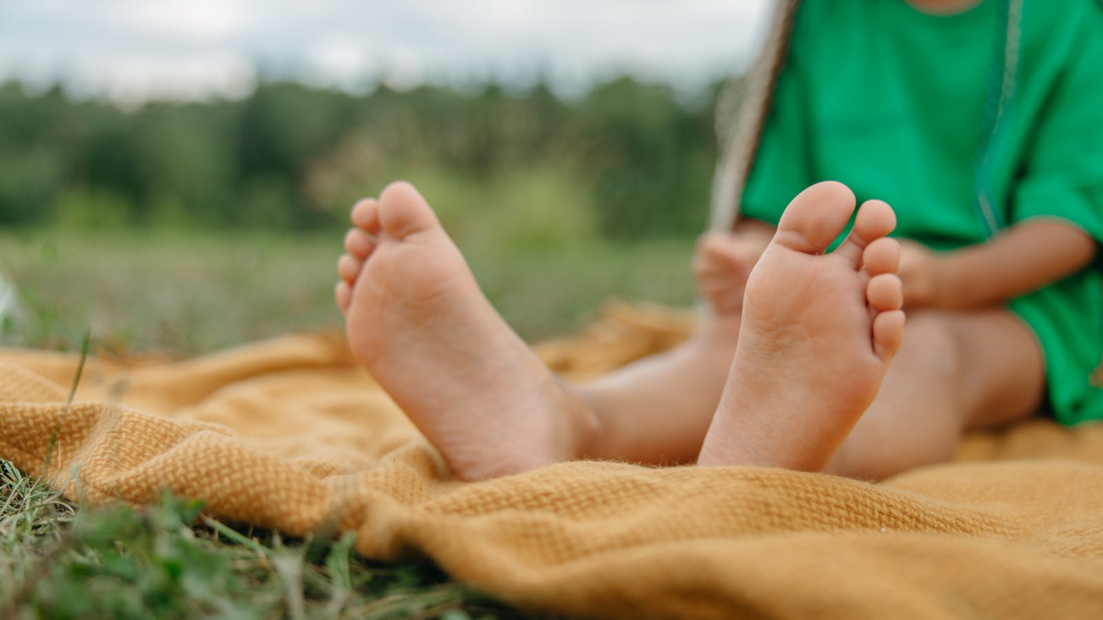 Close-up of a child's bare feet resting on a blanket outdoors.