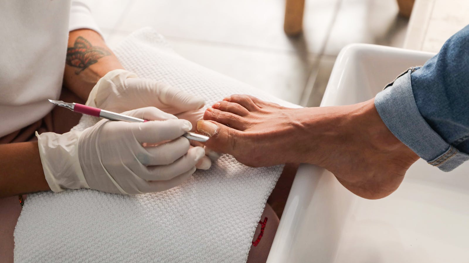 Gloved foot care provider using a professional tool while treating a thick toenail.